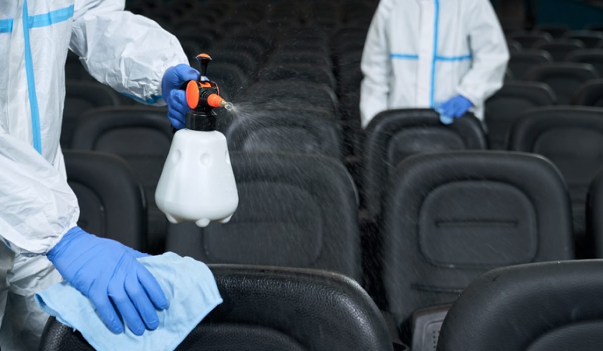 Two worker in protective clothes cleaning chairs in cinema hall with disinfectants. Concept of disinfection.